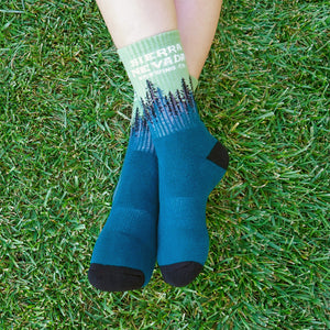 Thumbnail of A person wears a pair of the Sierra Nevada Treeline Socks while sitting on a grassy area