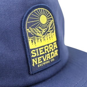 Thumbnail of Close-up of a navy blue baseball cap featuring a prominent yellow embroidered patch with a mountain and sun graphic and the text 'SIERRA NEVADA BREWING CO.'.
