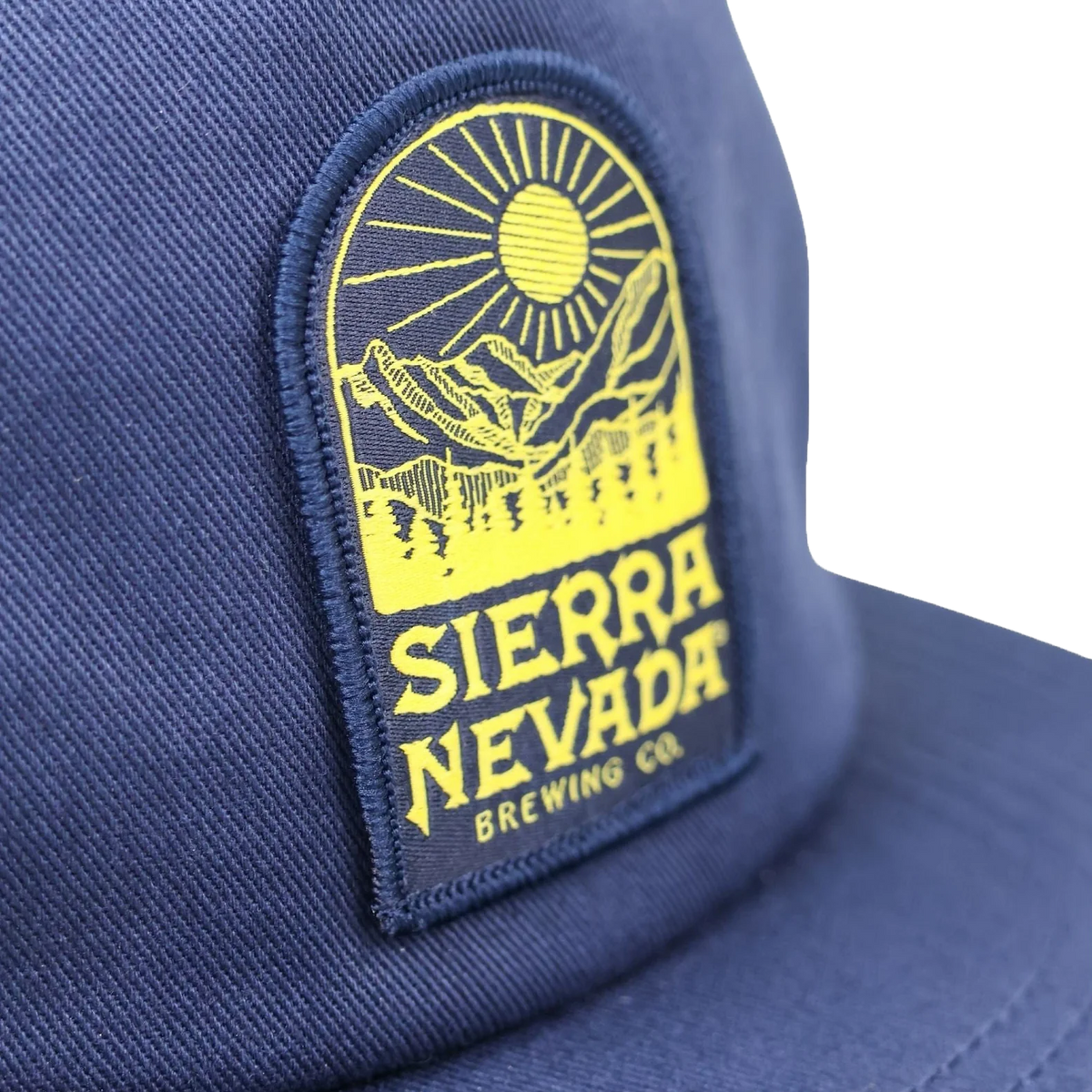Close-up of a navy blue baseball cap featuring a prominent yellow embroidered patch with a mountain and sun graphic and the text 'SIERRA NEVADA BREWING CO.'.