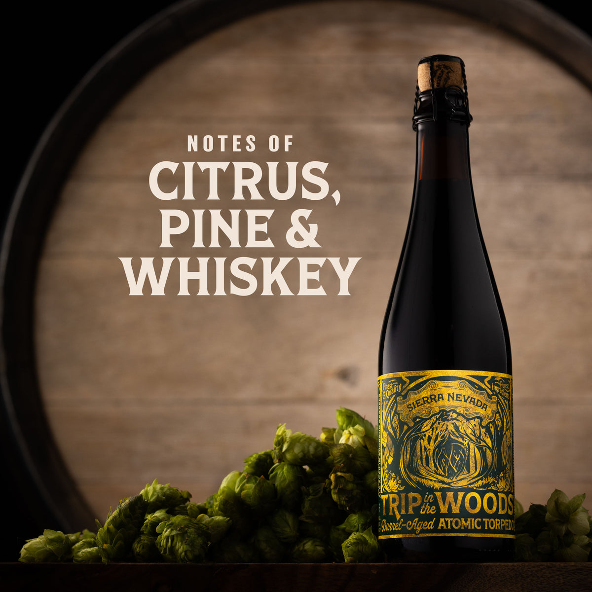 A dark glass bottle of Tripawoods Whiskey with a yellow label stands in front of a wooden barrel, with green hops piled at the base. White text on the left reads 'NOTES OF CITRUS, PINE & WHISKEY'.