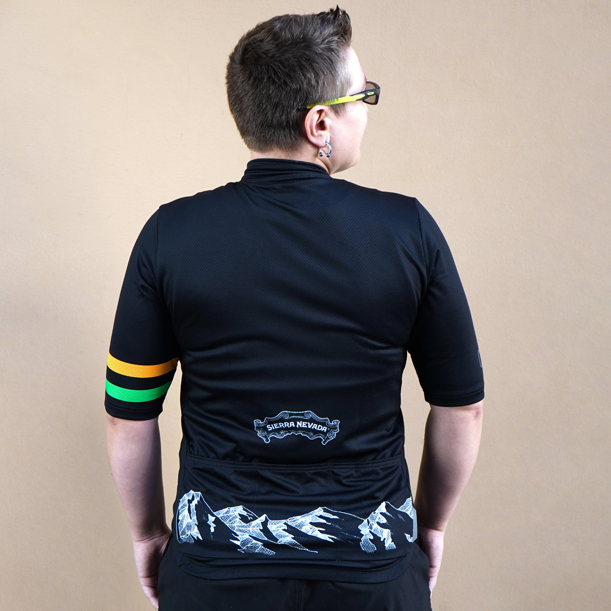 Person wearing a black cycling jersey with colorful stripes on the back against a beige background