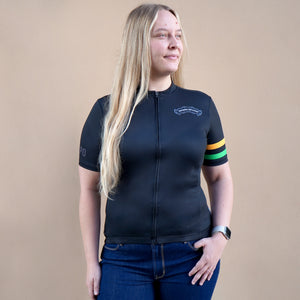 Thumbnail of Woman wearing a black cycling jersey with colorful arm stripes on a beige background