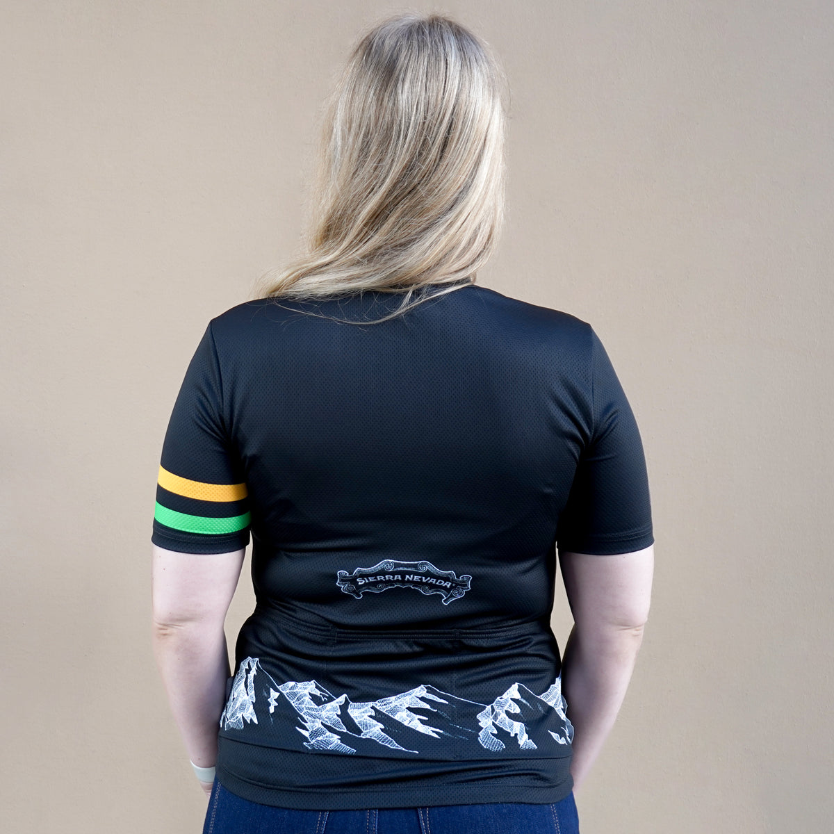 Person wearing a black t-shirt with mountain design on the back, standing against a beige background