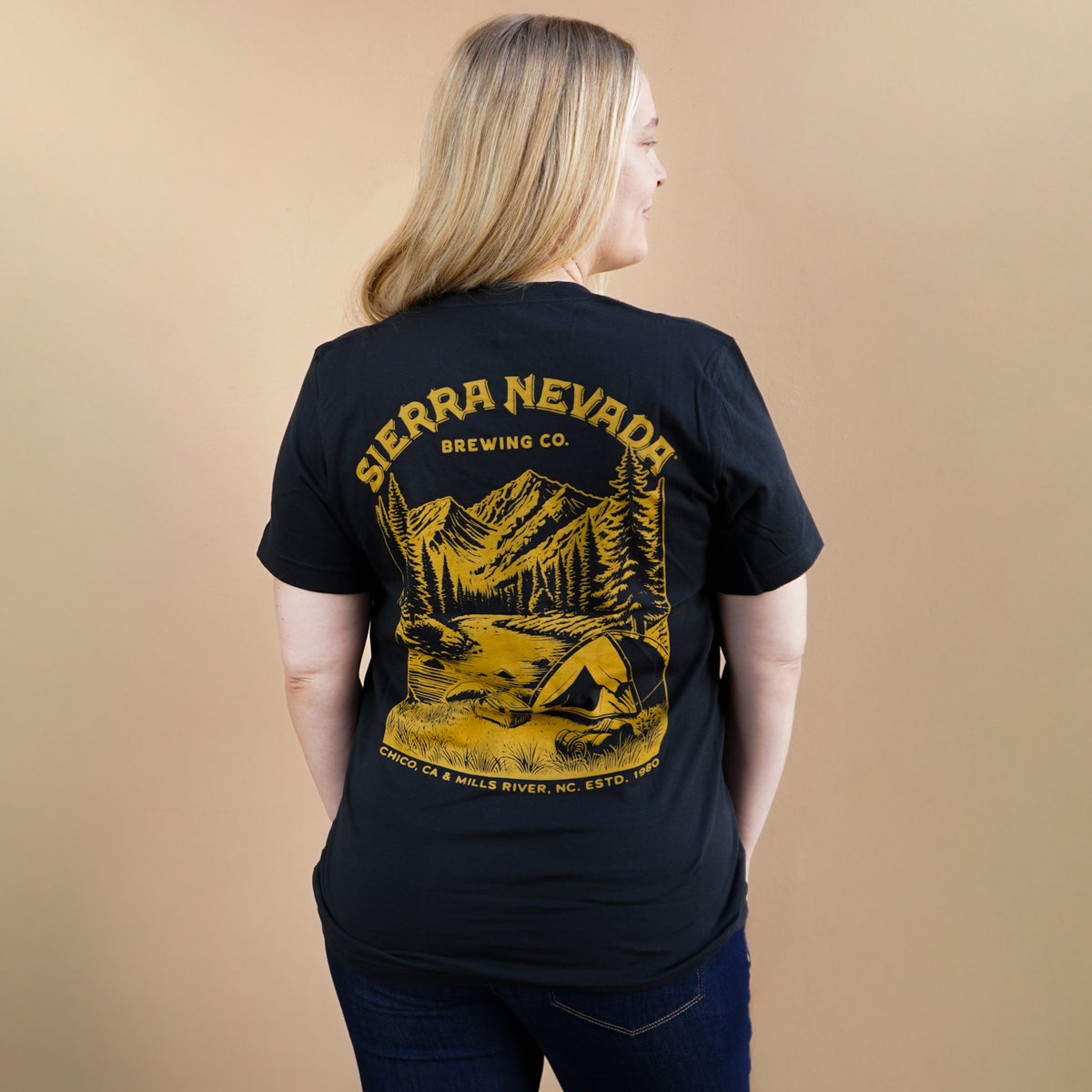 Person wearing a black t-shirt with yellow Sierra Nevada Brewing Co. logo on the back against a beige background