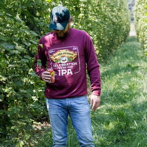 Thumbnail of Man in a purple sweatshirt and blue jeans standing in a field holding a beer.