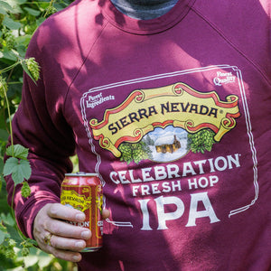 Thumbnail of Person wearing a Sierra Nevada Celebration Fresh Hop IPA sweatshirt holding a beer can in a garden setting.