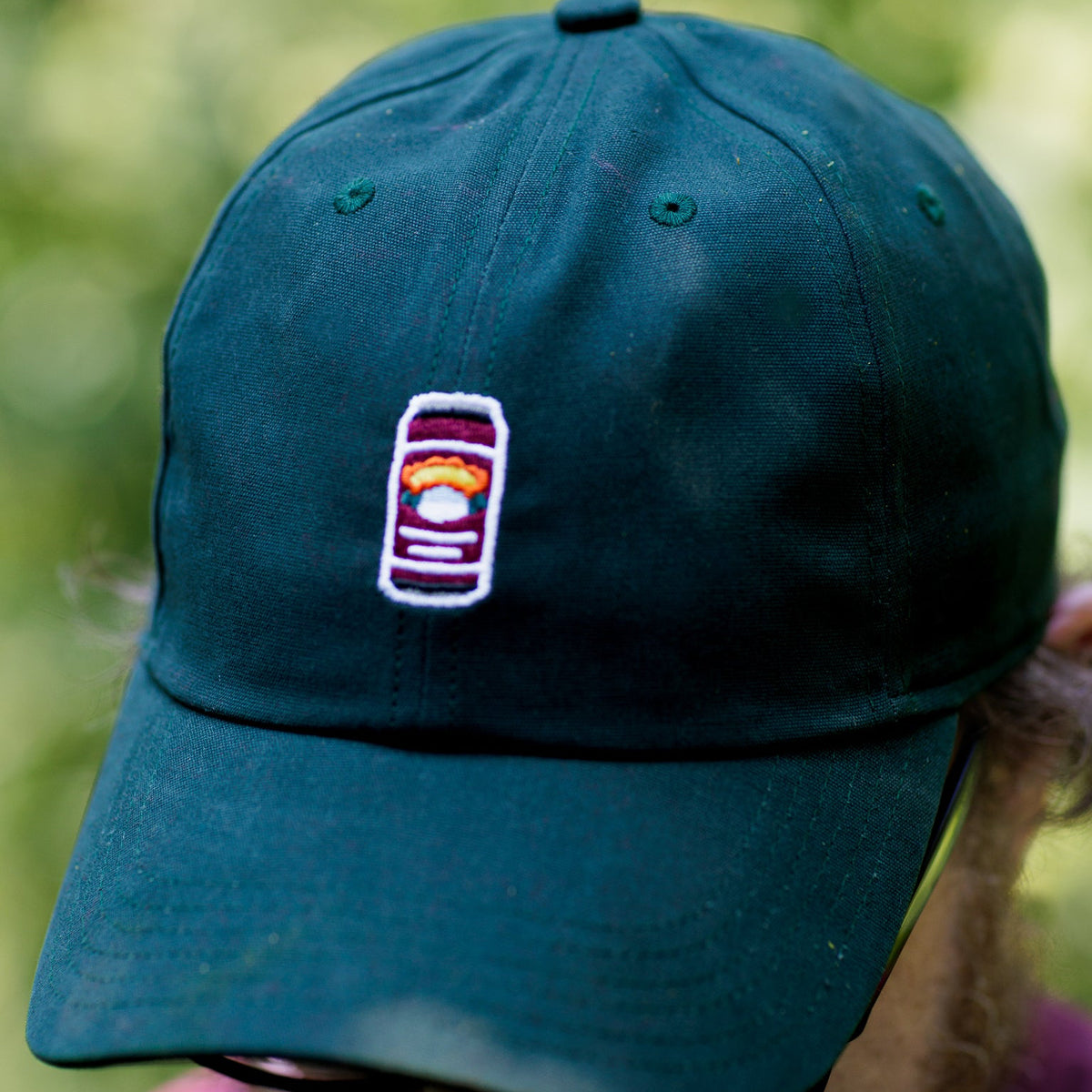 Green cap with a logo worn by a person against a blurred green background