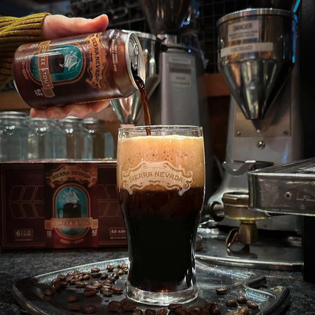 Sierra Nevada Coffee Stout poured into a pint glass in front of roasting machinery