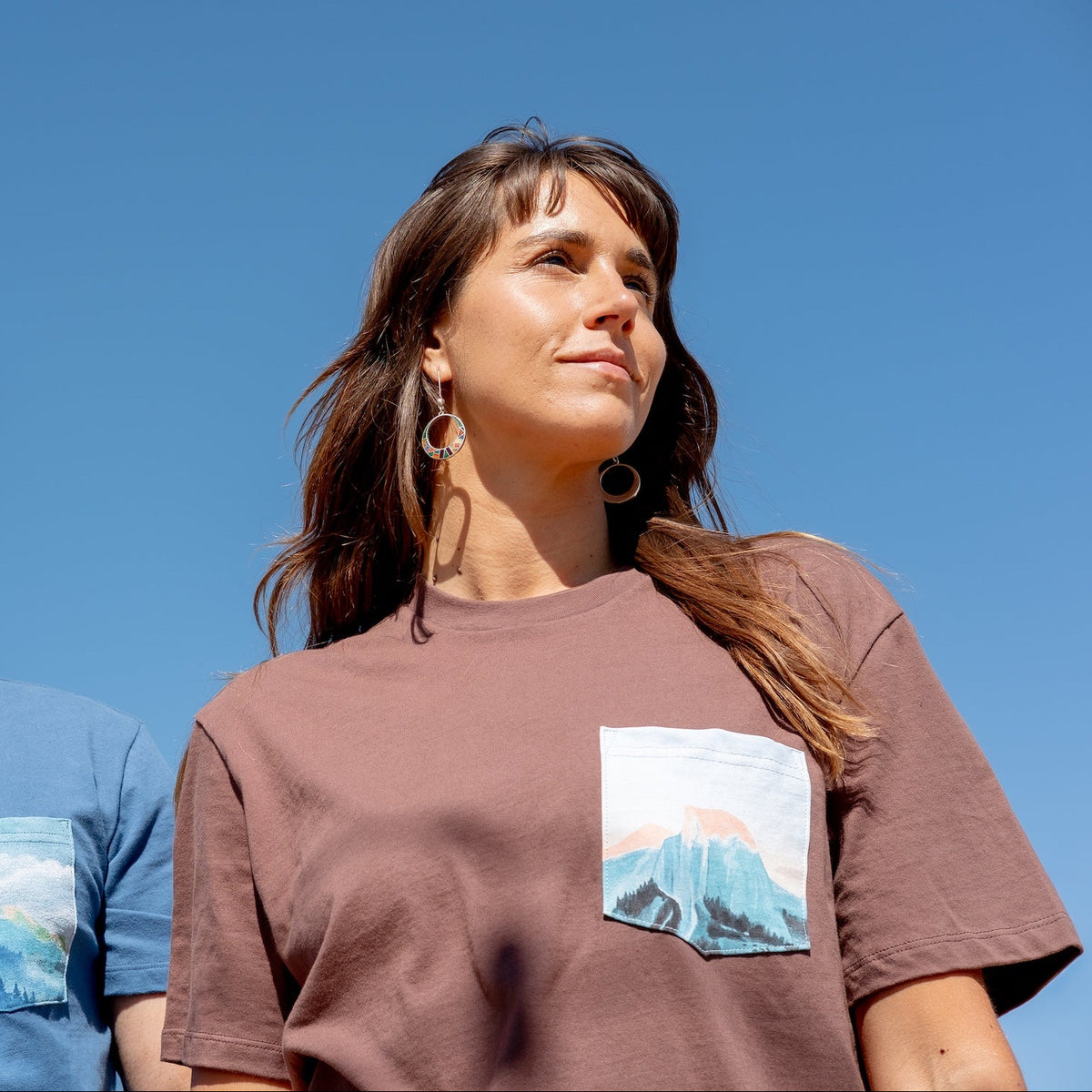Two people wearing t-shirts with mountain designs against a clear blue sky.