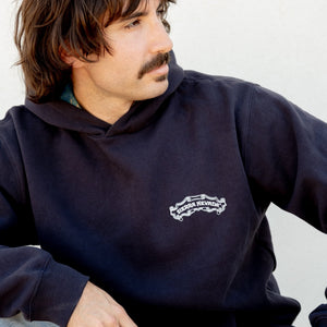 Thumbnail of Man wearing a navy hoodie with a logo, sitting against a plain background