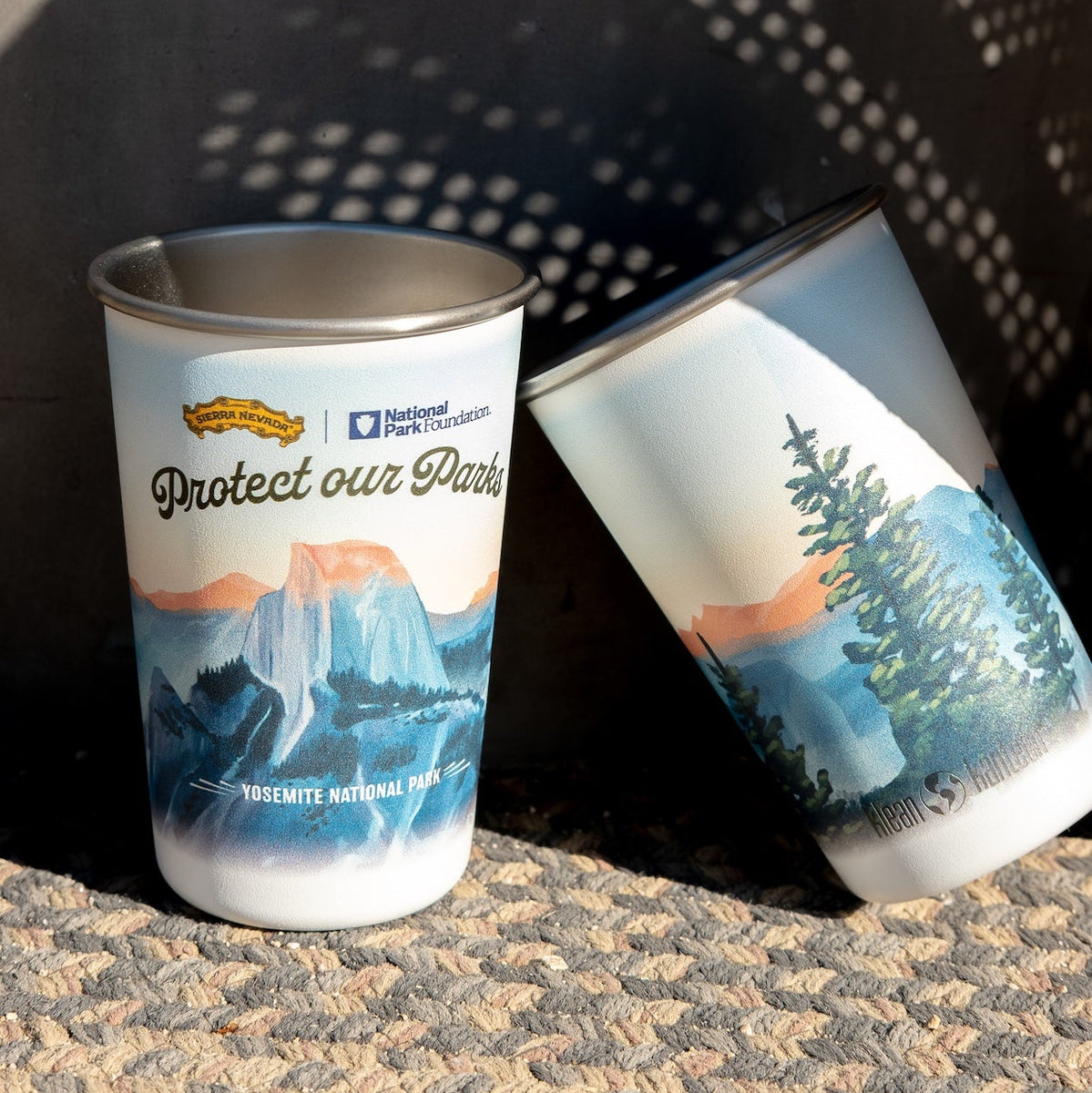Two stainless steel cups with nature-themed designs and text on a textured surface.