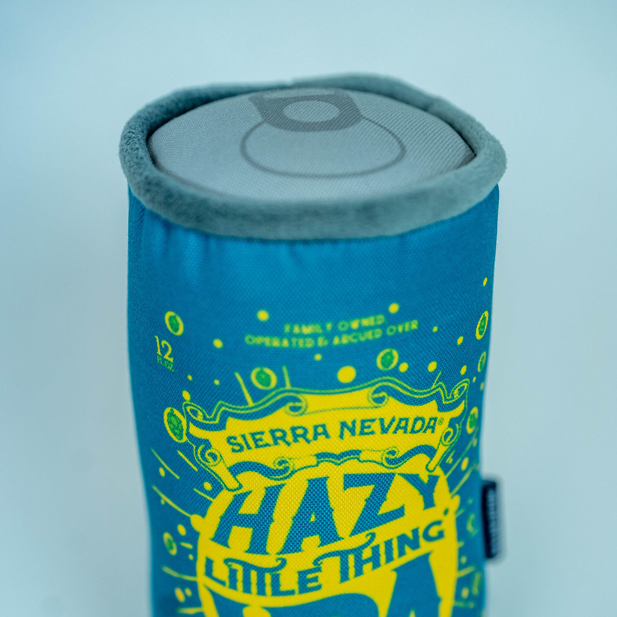 A plush can-shaped can cooler featuring a blue and yellow design with 'SIERRA NEVADA HAZY LITTLE THING IPA' printed on it, set against a light blue-gray background.