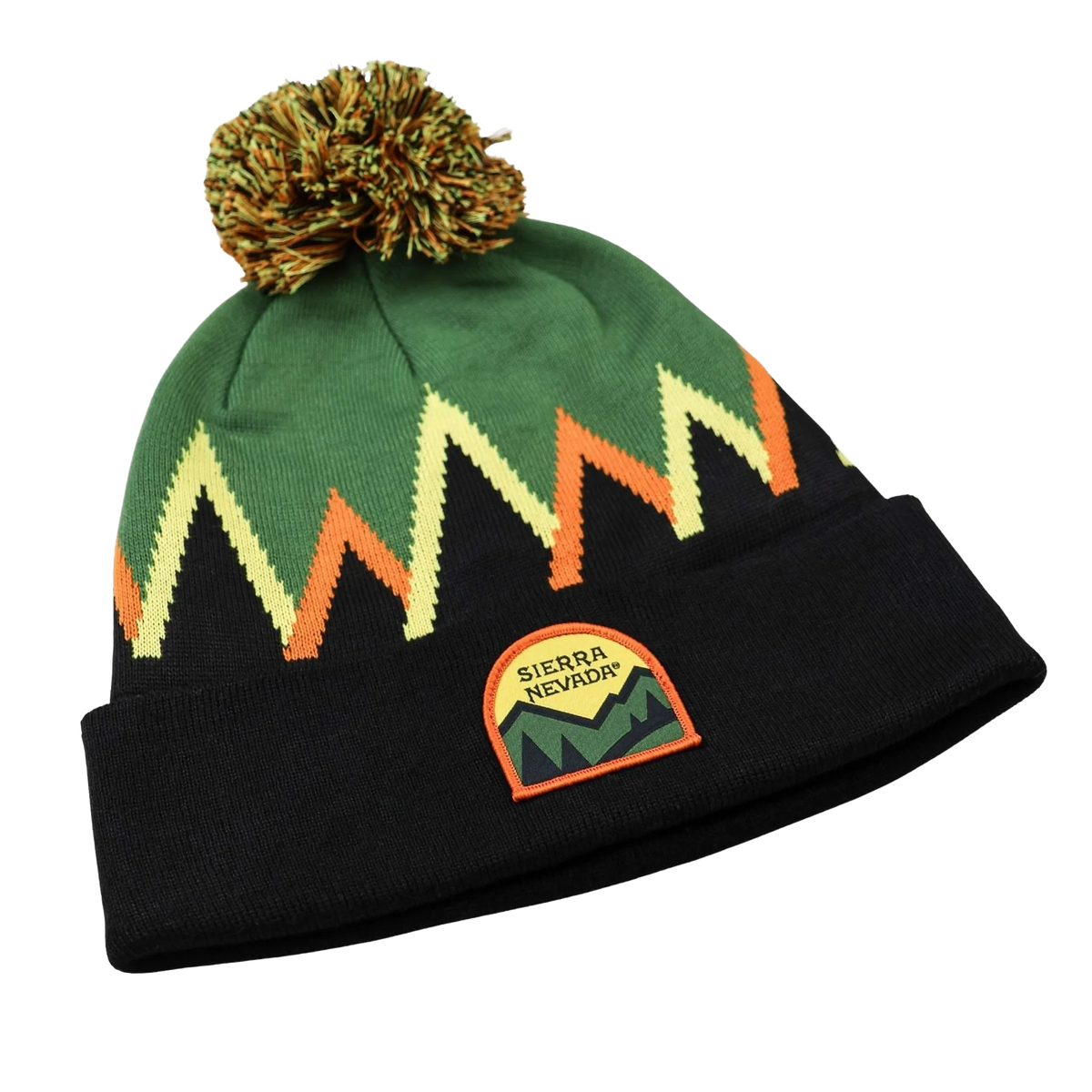 A knit pom-pom beanie hat featuring a green upper section with a zigzag pattern in cream, orange, and black, a black cuff, and a Sierra Nevada mountain patch on the front.