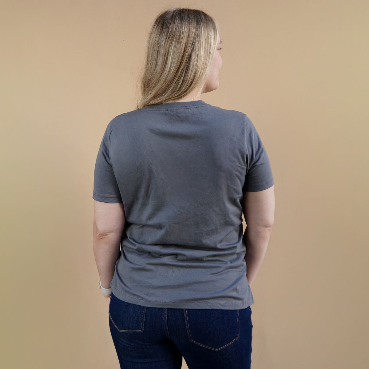 Person wearing a gray t-shirt and dark jeans against a beige background