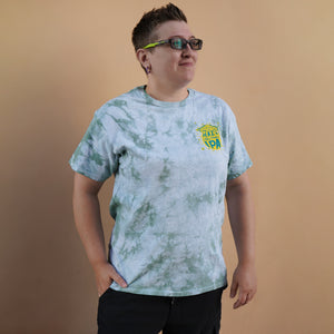 Thumbnail of Person wearing a tie-dye t-shirt with a logo on a brown background