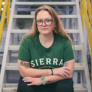 Thumbnail of Person wearing a green 'SIERRA' t-shirt standing in front of a staircase.