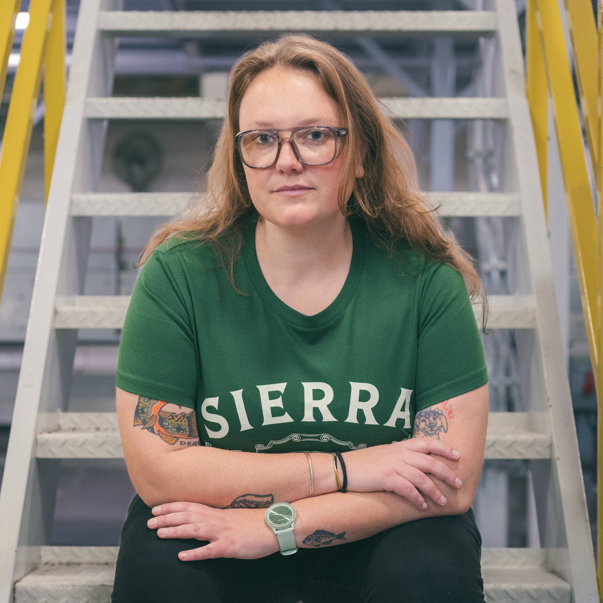 Person wearing a green 'SIERRA' t-shirt standing in front of a staircase.