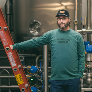 Thumbnail of Person wearing a green Sierra Nevada Brewing Co. sweatshirt standing in a brewery setting with brewing equipment.