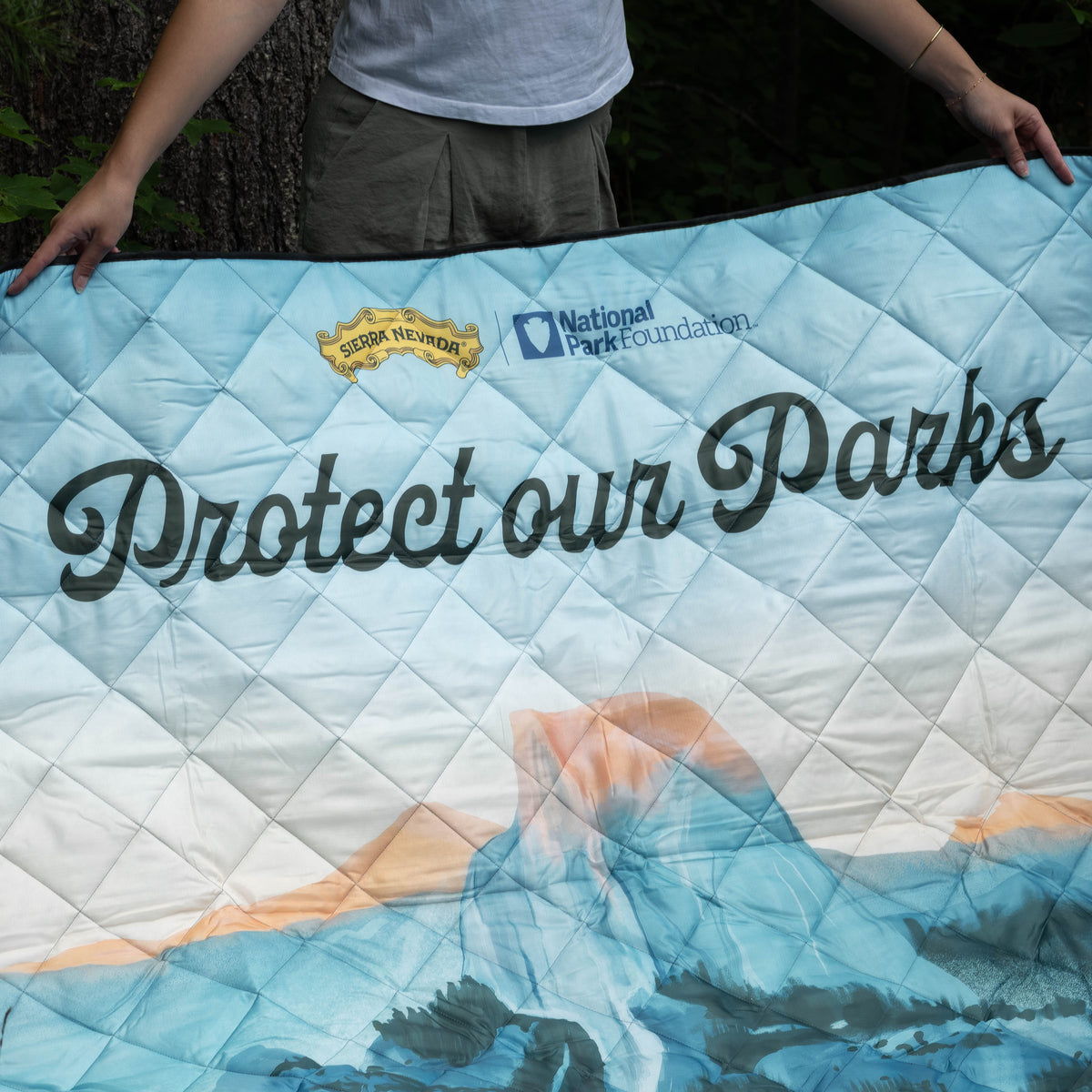 Person holding a quilt with 'Protect our Parks' and National Park Foundation branding.