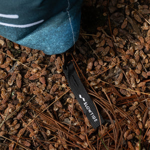 Thumbnail of Close-up of the corner of the NPF X Sierra Nevada packable blanket with a visible brand logo on a pine cone-strewn ground.