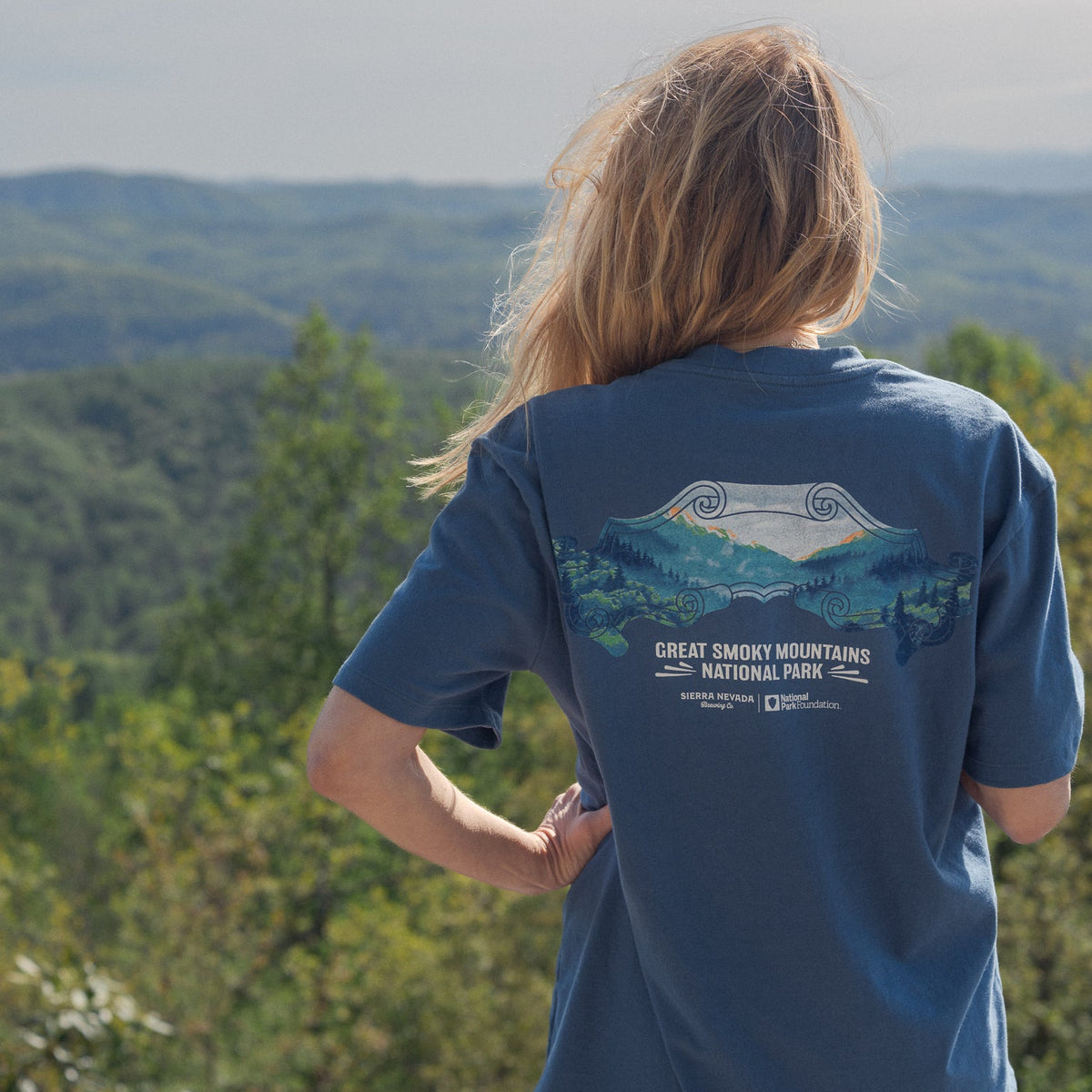 Person wearing a blue t-shirt with a national park design, standing in front of a scenic view.