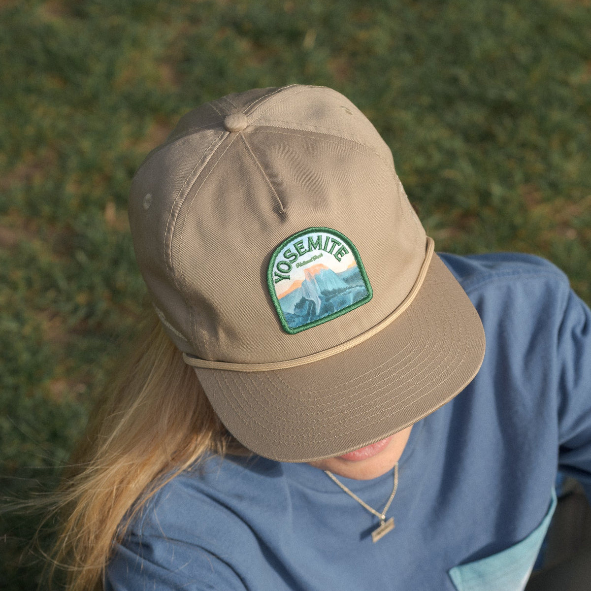 Person wearing a beige cap with Yosemite National Park patch in a grassy area