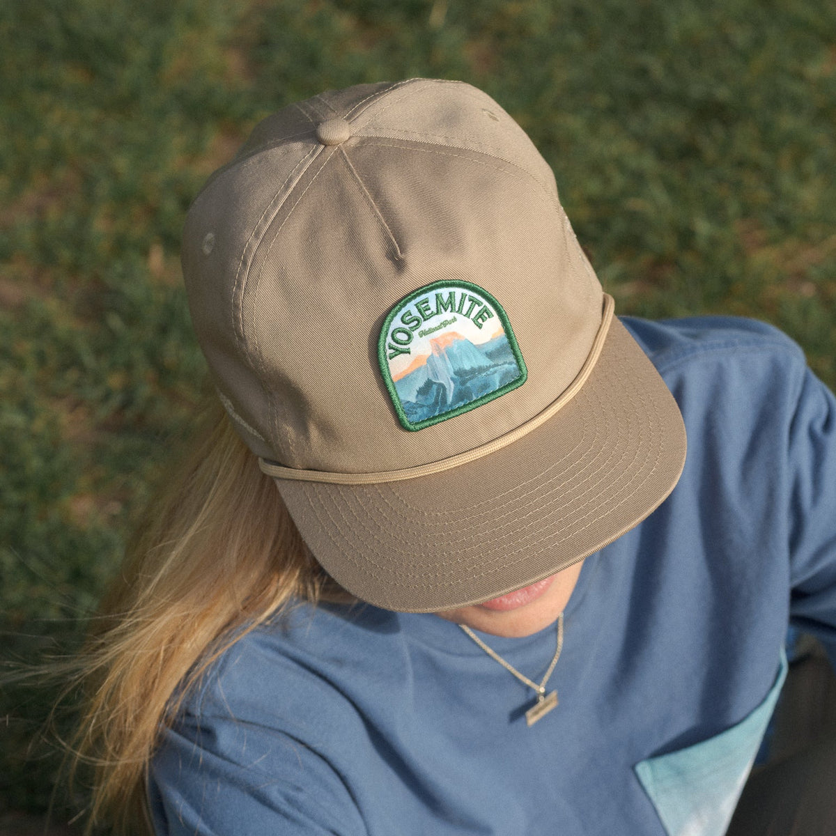 Person wearing a beige cap with Yosemite National Park patch in a grassy area