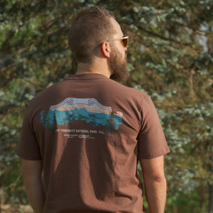 Thumbnail of Man wearing a brown t-shirt with a nature graphic, standing in a forested area.