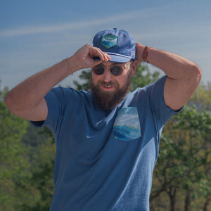 Thumbnail of Man wearing a blue cap and sunglasses with a scenic background