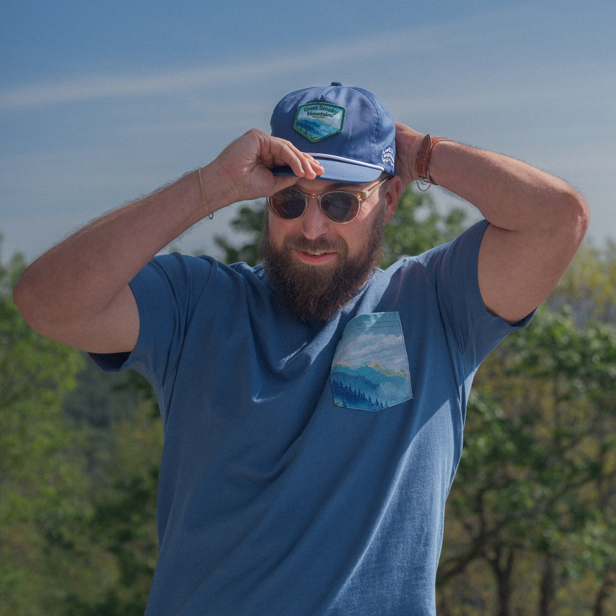 Man wearing a blue cap and sunglasses with a scenic background