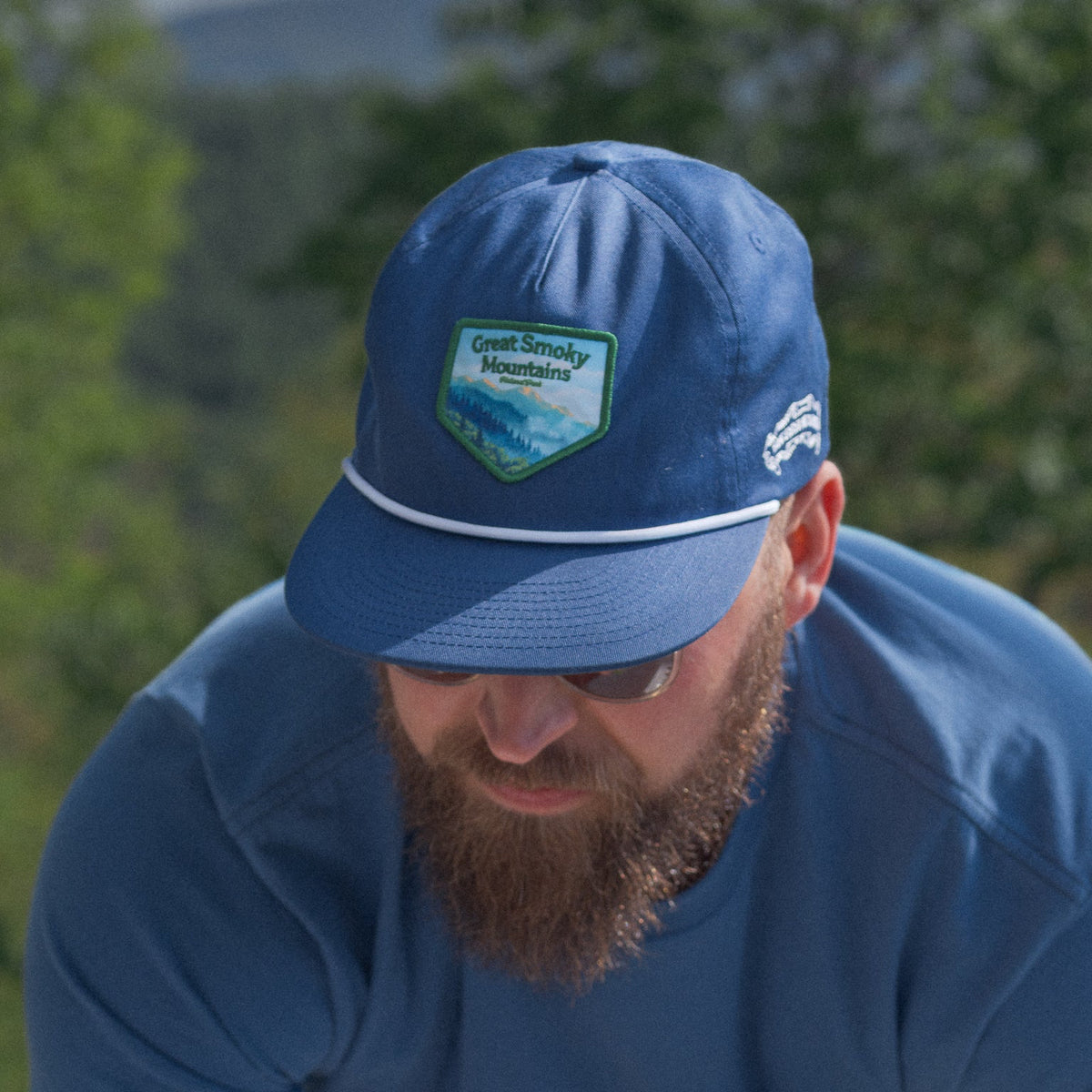 Man wearing a blue cap and shirt outdoors with greenery in the background