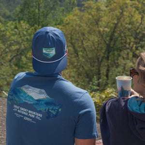 Thumbnail of Two people wearing blue shirts with mountain designs, looking at a scenic view of trees and mountains.