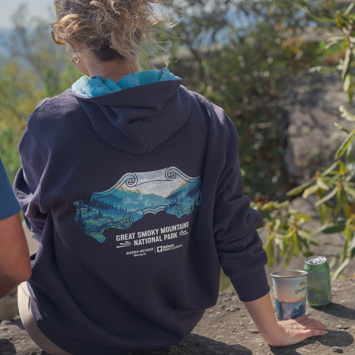 Person wearing a Great Smoky Mountain National Park hoodie sitting outdoors with a scenic background.