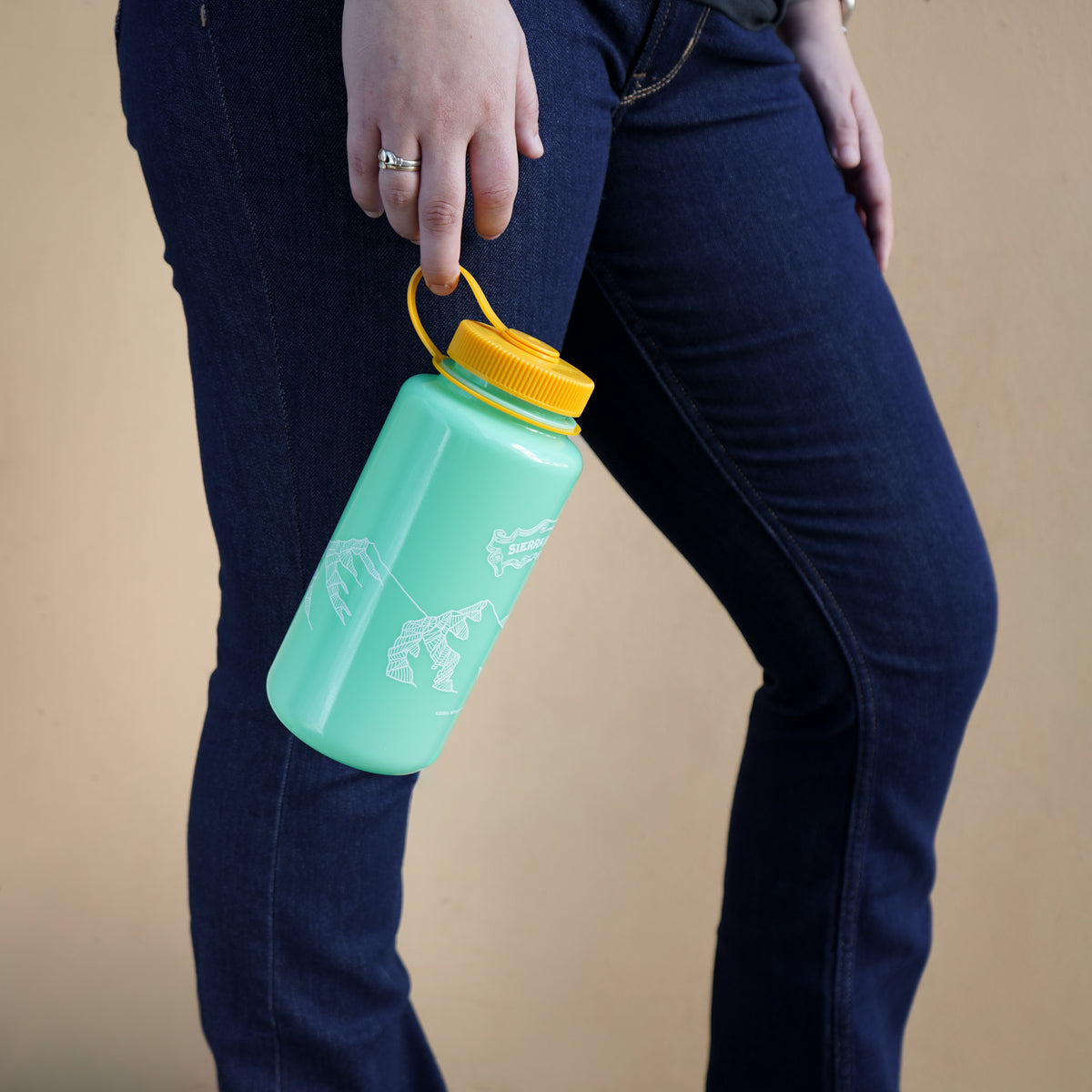 Person holding a green water bottle with a yellow cap against a beige background