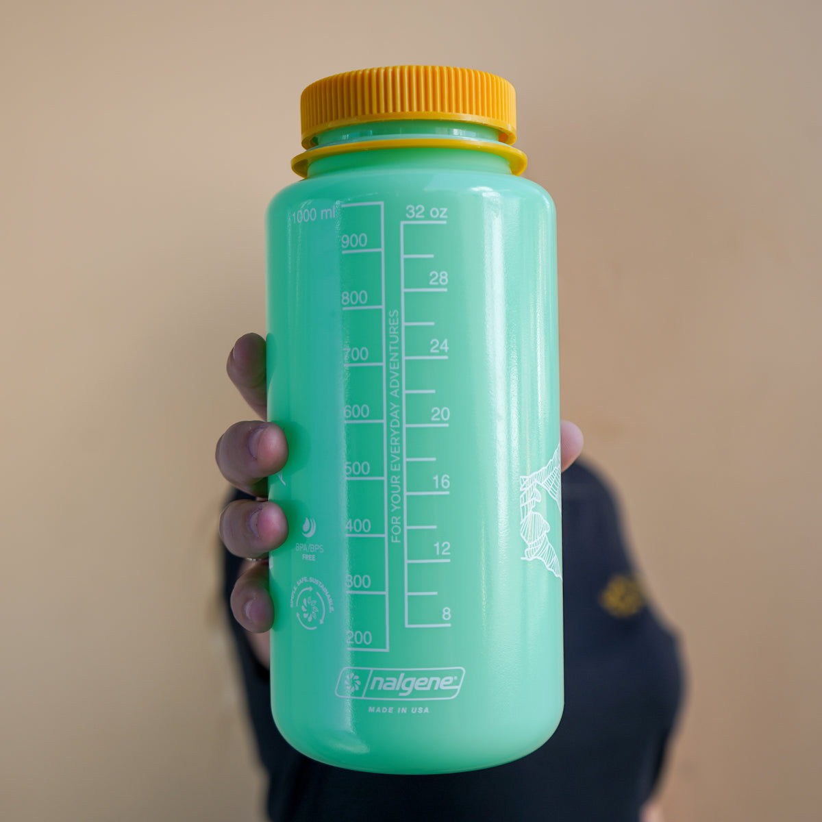 Green Nalgene bottle with yellow cap held against a beige background