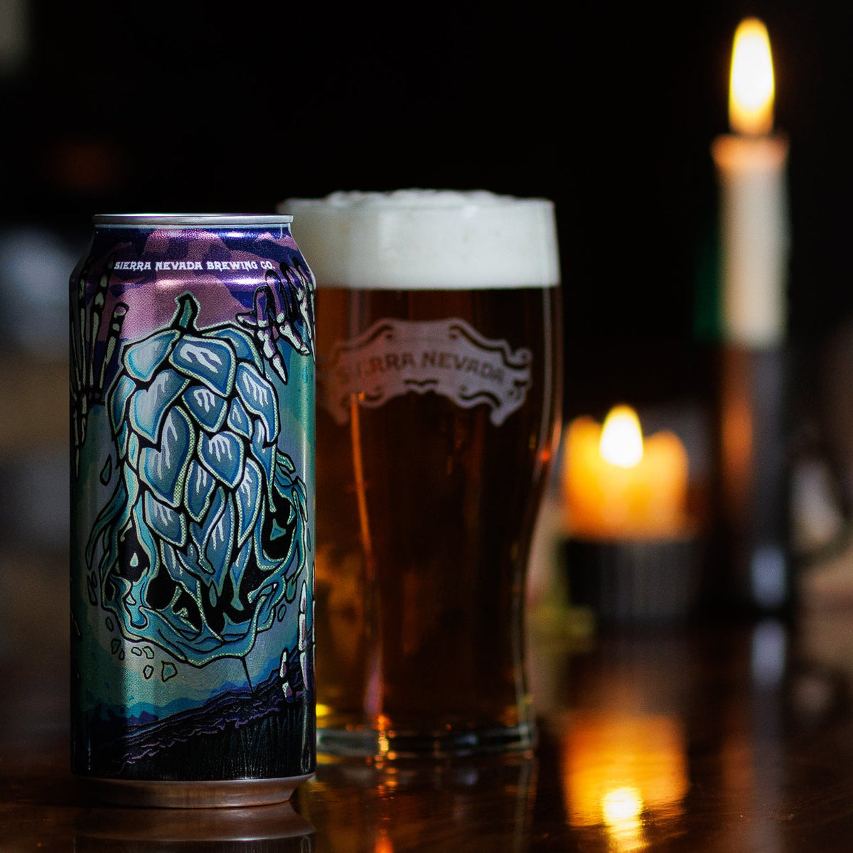 Beer can and pint glass on a bar with candles in the background