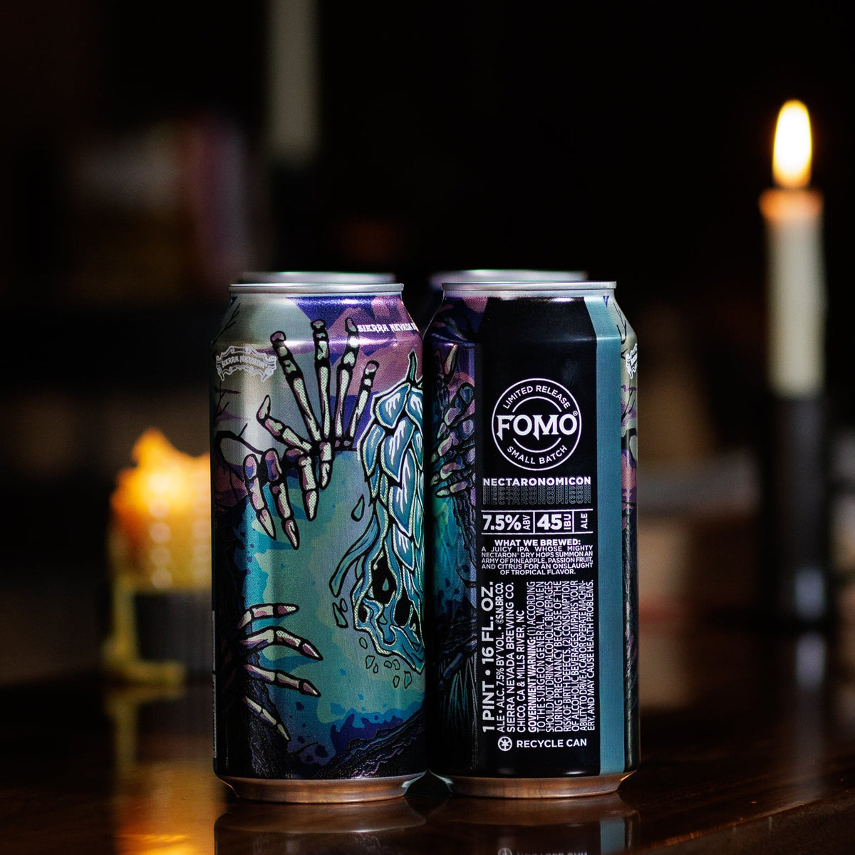 Two beer cans with artistic designs on a dark background with candles.