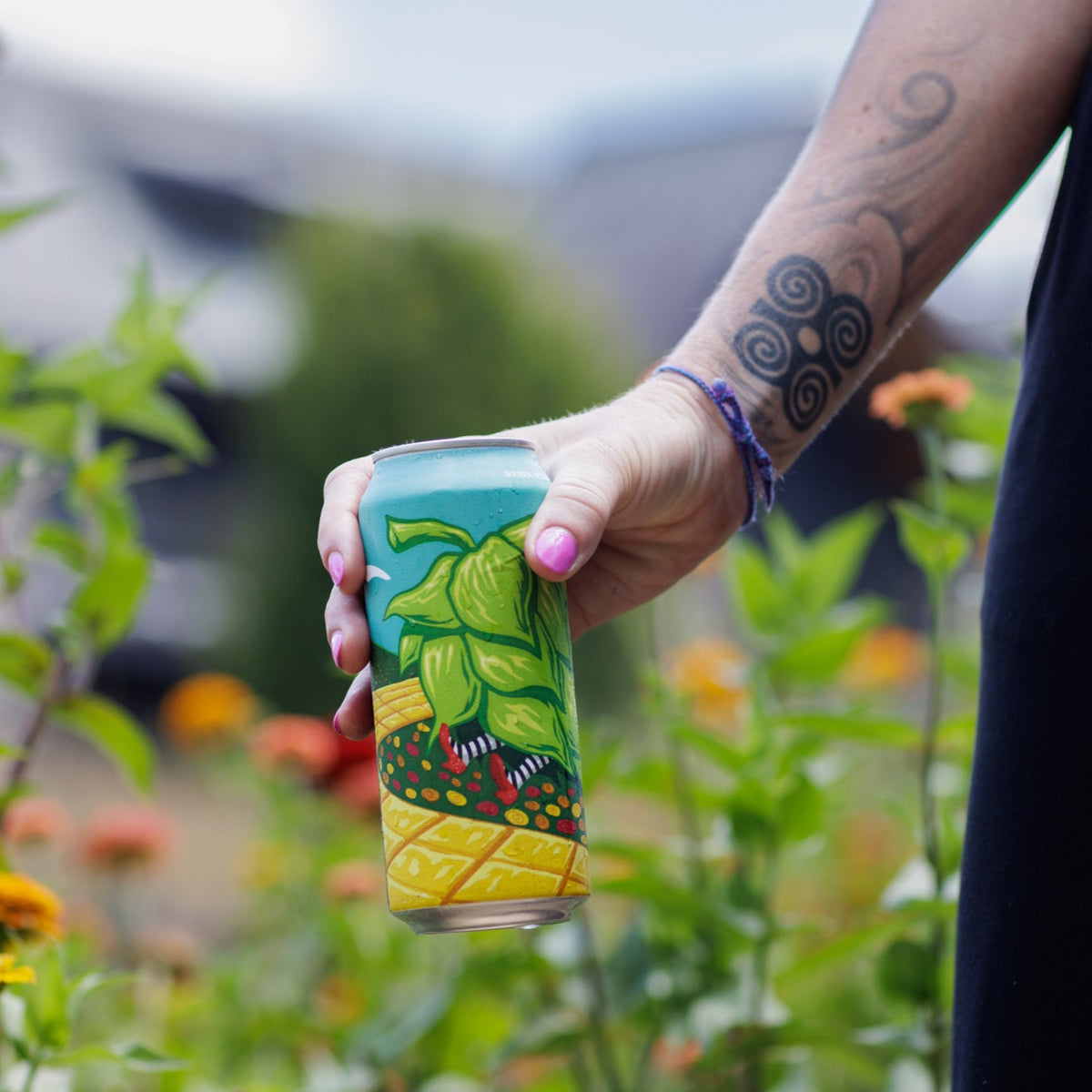 Person holding a colorful beer can with a garden in the background