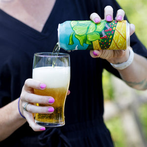 Thumbnail of Person pouring beer from a colorful can into a glass outdoors.