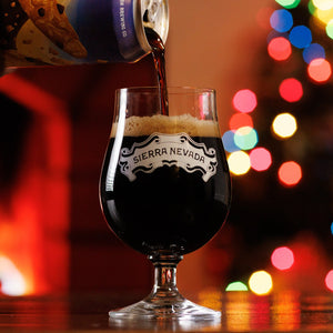 Thumbnail of A can of Oatmeal Cookie Stout is poured into a balloon glass with festive holiday lights in the background