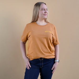 Thumbnail of Person wearing an orange t-shirt with a logo on a beige background