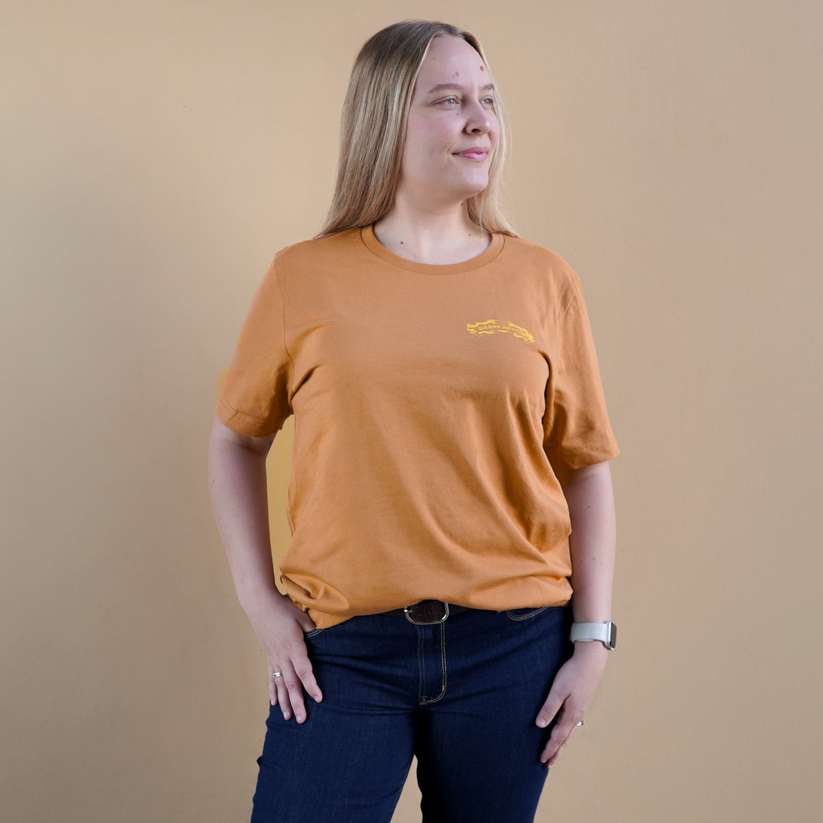 Person wearing an orange t-shirt with a logo on a beige background
