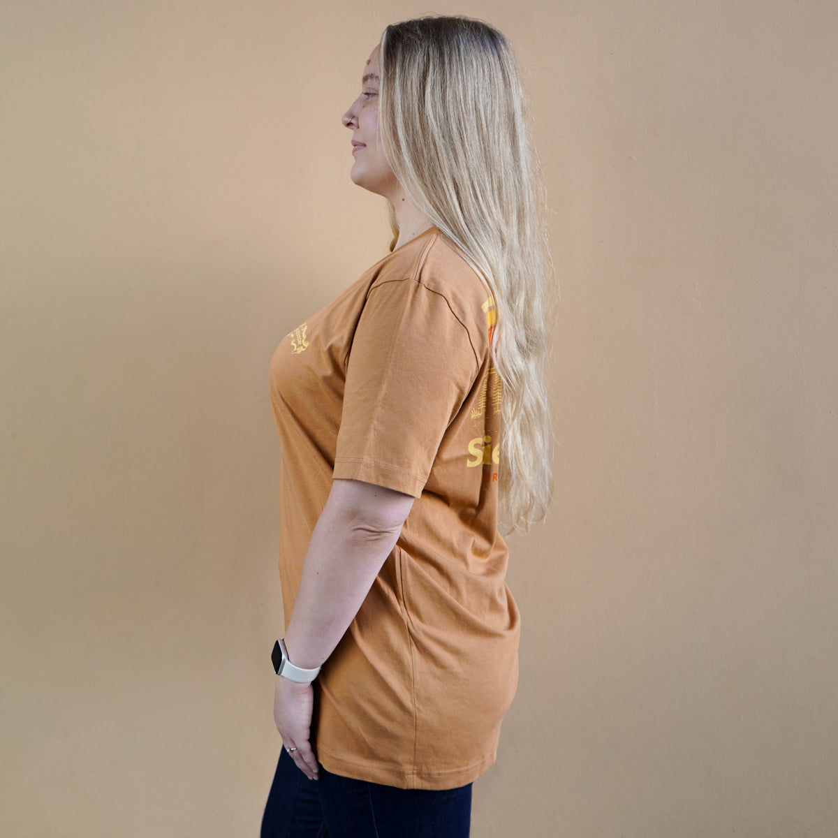 Person wearing a brown t-shirt with visible branding on a beige background