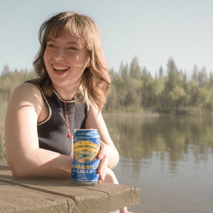 Thumbnail of Person holding a can by a lake with trees in the background