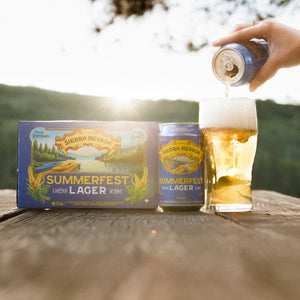 Thumbnail of Person opening a beer bottle of Sierra Nevada Summerfest Lager on a wooden surface with a scenic background.