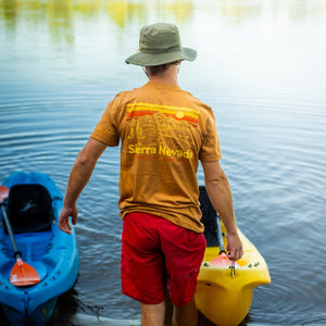 Thumbnail of Man in a yellow shirt and red shorts standing by two kayaks on a lakeshore.