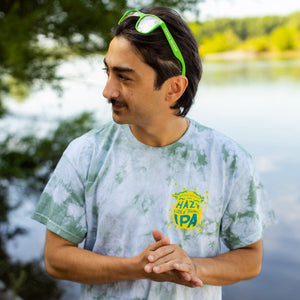 Thumbnail of Man wearing a tie-dye shirt with a logo by a lake