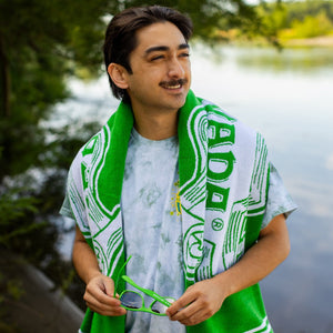 Thumbnail of A man stands by a river with the Sierra Nevada beach towel around his shoulders.