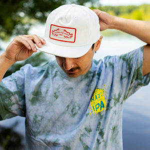 Thumbnail of Person wearing a white cap with a red logo and a tie-dye shirt with visible branding.