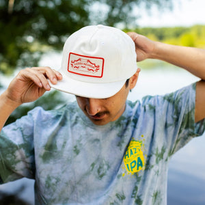 Thumbnail of Person wearing a white cap with a red logo and a tie-dye shirt with visible branding.